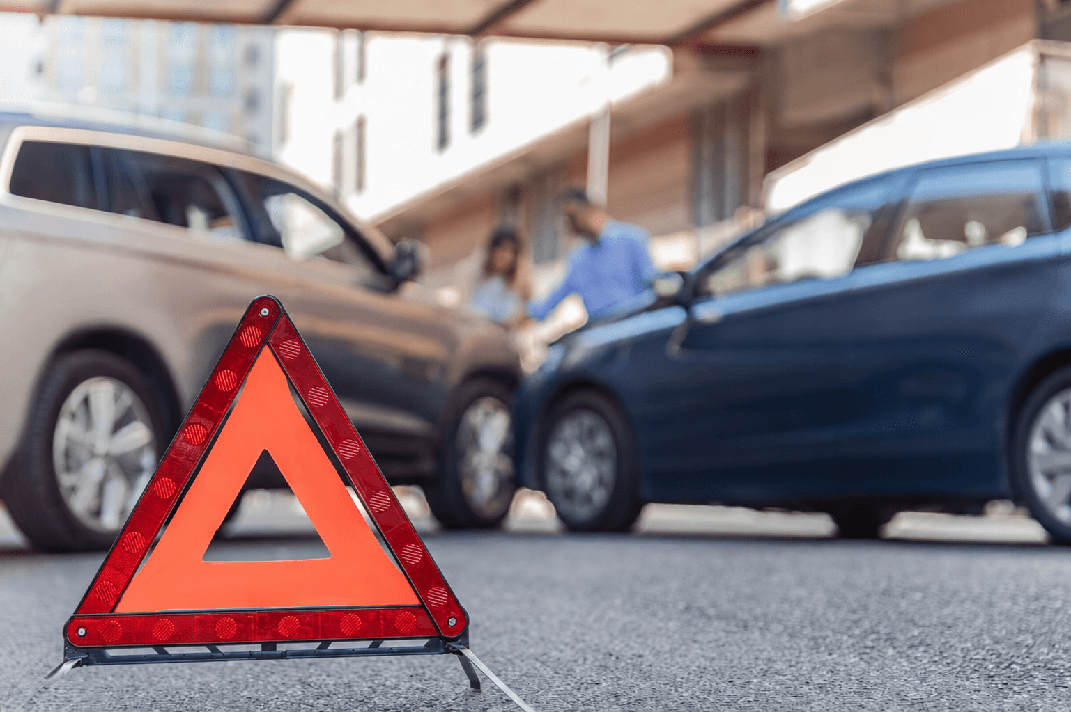 Warndreieck nach einem Verkehrsunfall, im Hintergrund tauschen zwei Unfallbeteiligte ihre Daten aus